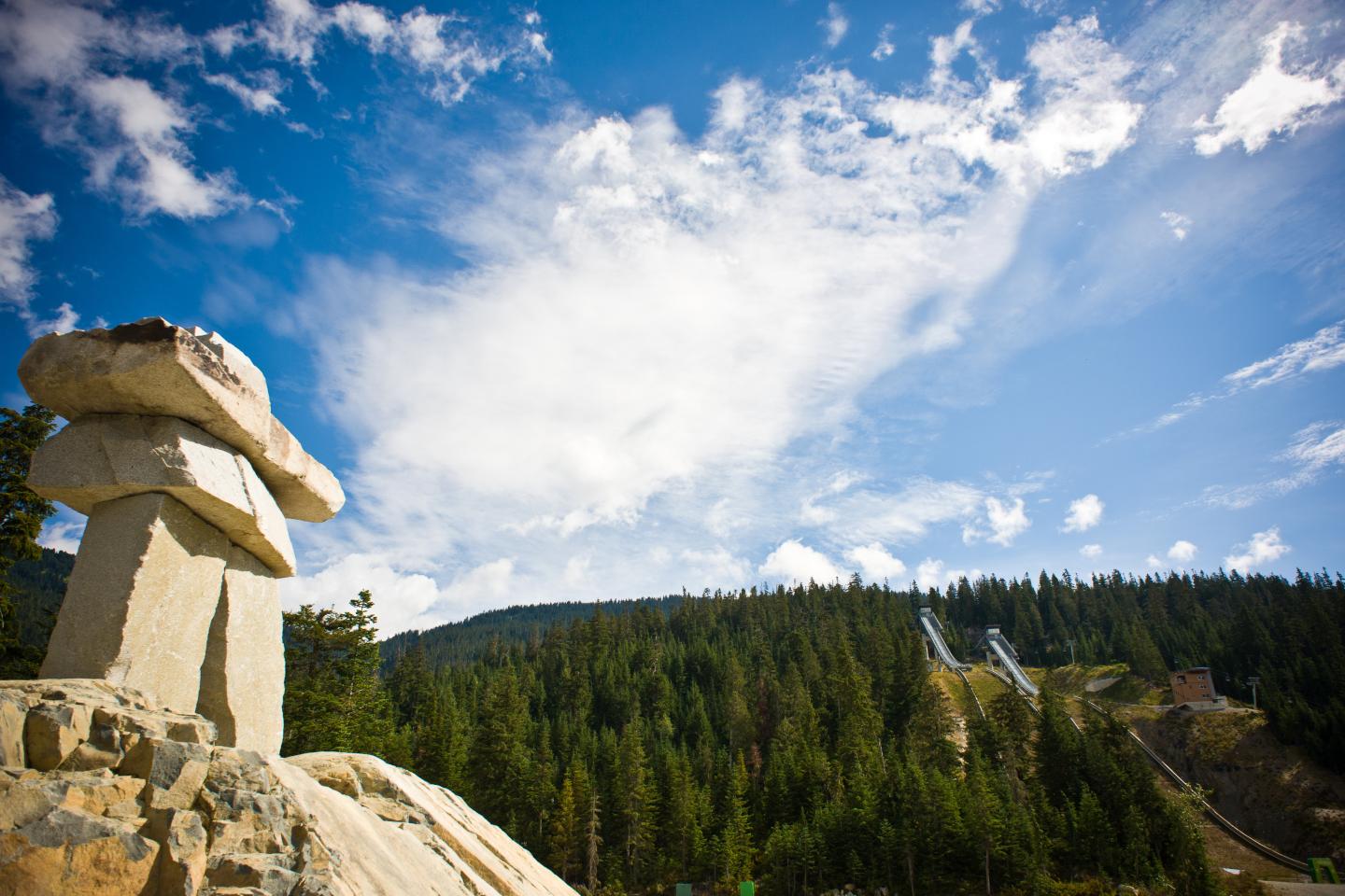Image looking up at inukshuk with sky, clouds, and mountains behind it