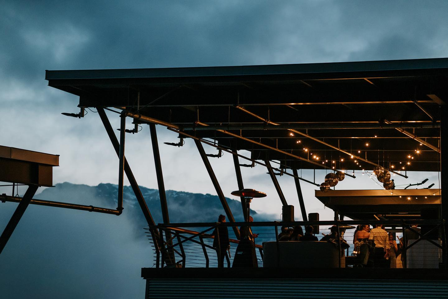 Rooftop bar with string lights at dusk, overlooking misty hills.